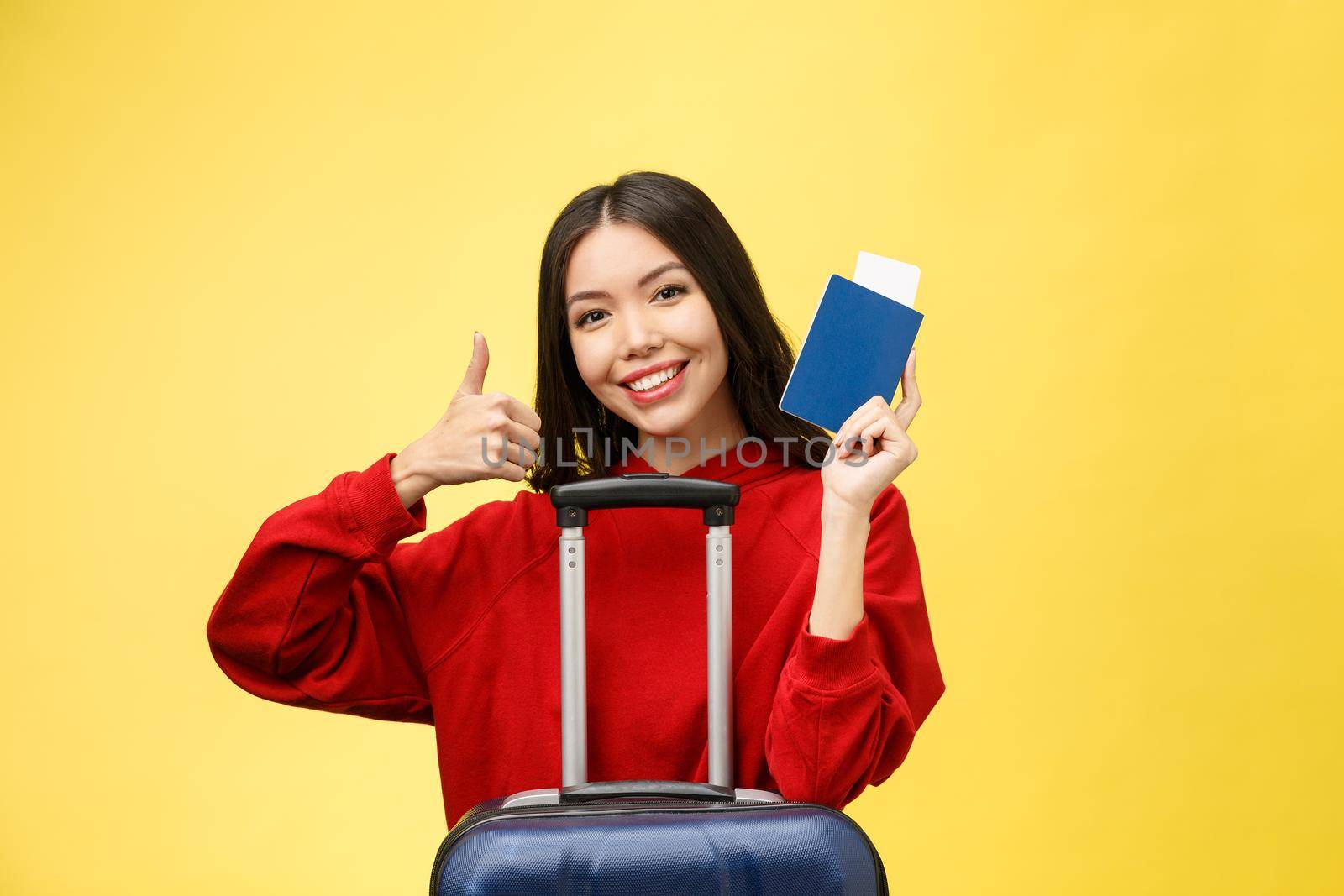 Woman travel. Young beautiful asian woman traveler with passport and suitcase on yellow background.