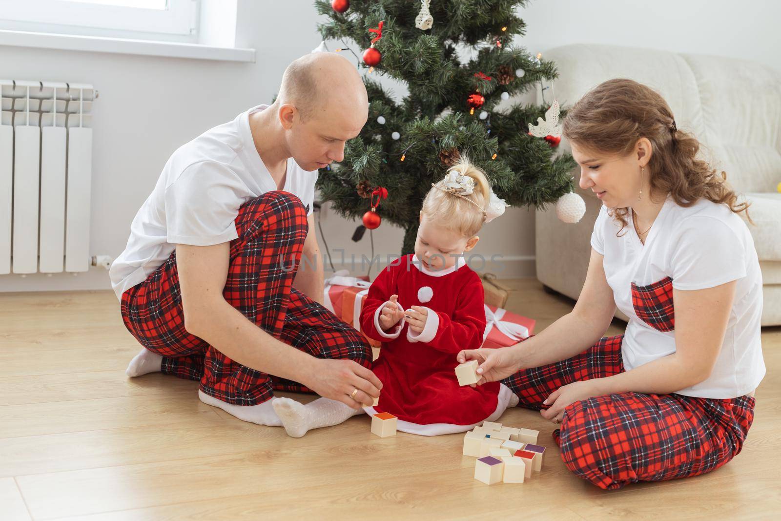 Toddler child with cochlear implant plays with parents under christmas tree - deafness and innovating medical technologies for hearing aid and diversity by Satura86