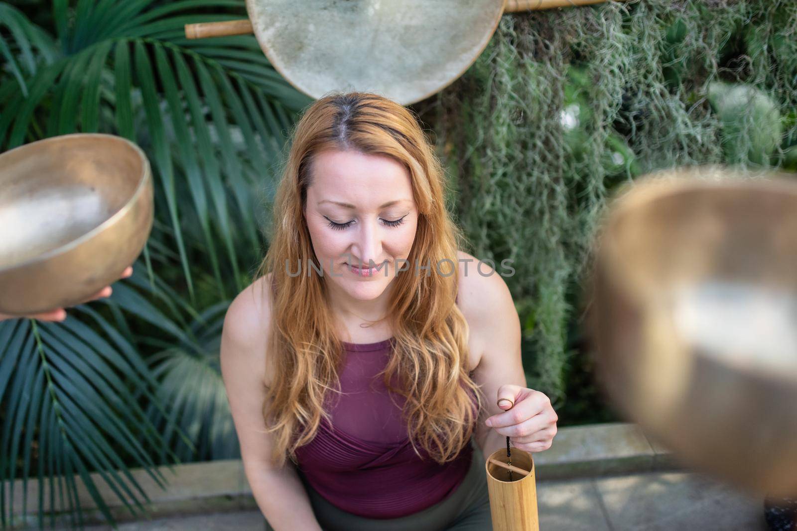 Yoga concept, meditation and sound therapy. Beautiful young caucasian woman surrounded by copper tibetan singing bowls and instruments