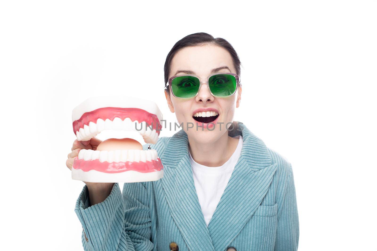 cute surprised woman in green glasses and a jacket holds a large dental jaw in her hand by shilovskaya