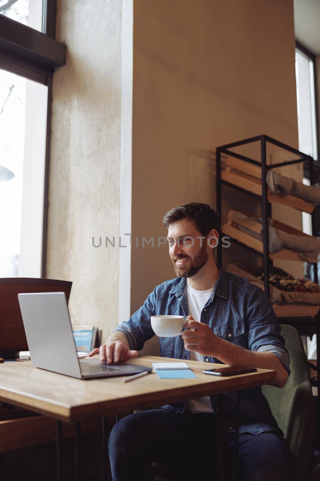 Happy caucasian young attractive man with cup of coffee sitting at laptop in cafe. Videocall concept