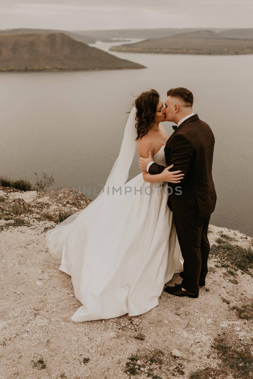 loving couple wedding newlyweds outdoor. bride in white dress long veil and groom in suit walk in summer fall on mountain above river. sunrise. man and woman on rocks above cliff. bakota ukraine