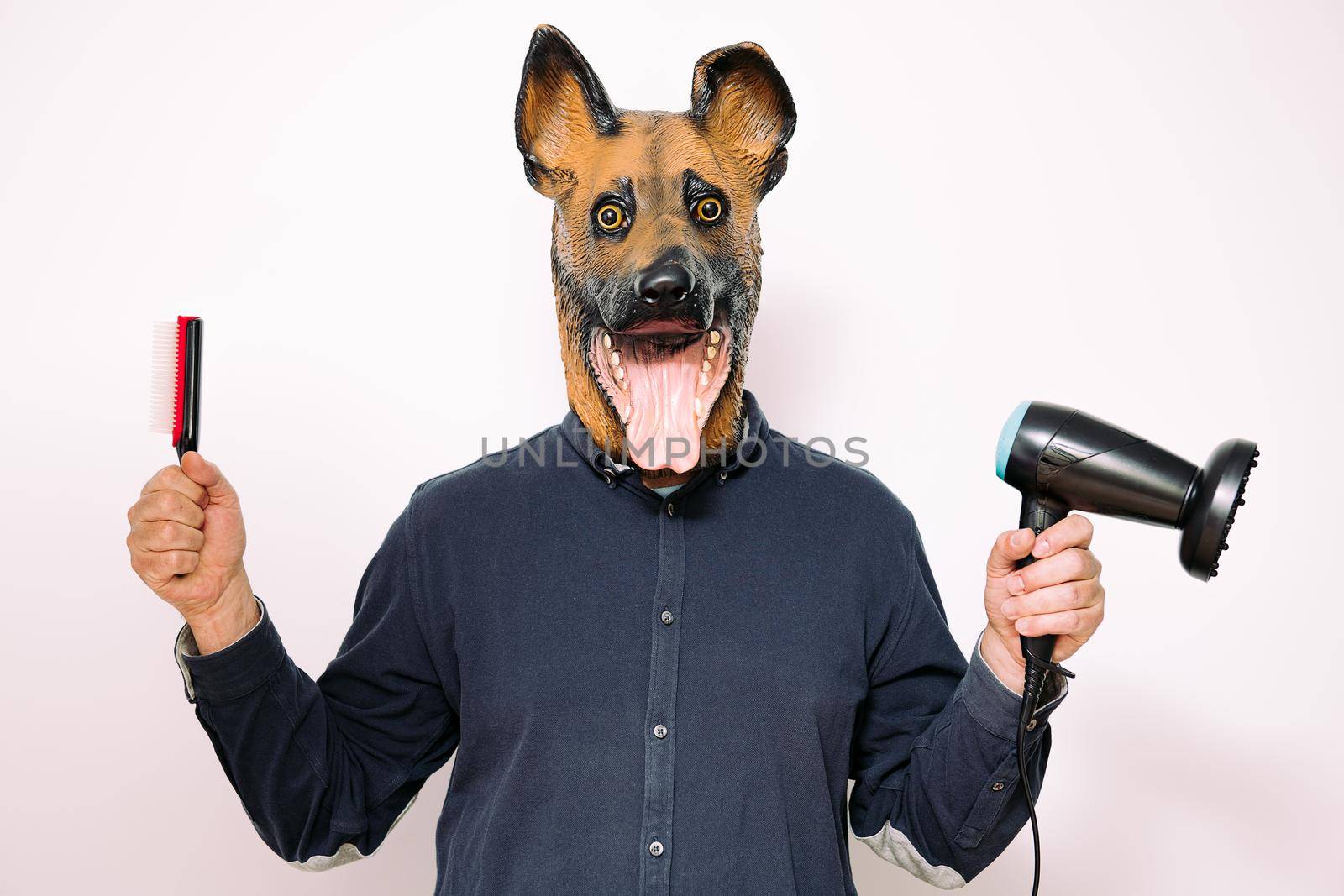 person with a dog mask holding a hairbrush and a hairdryer on white background, concept of hairdressing and grooming of pets