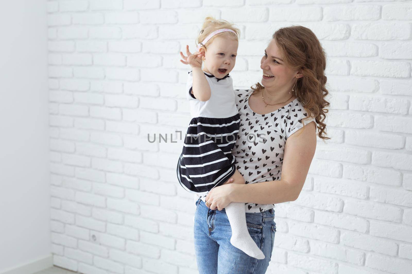 Mother holds and having fun her child with hearing aids and cochlear implants on white brick wall with copy space and place for advertising . Deaf and innovating medicine technologies concept by Satura86