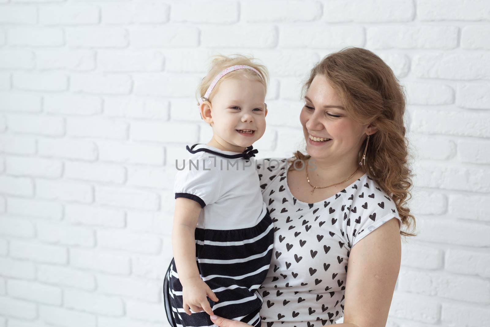 Mother holds and having fun her child with hearing aids and cochlear implants on white brick wall with copy space and place for advertising . Deaf and innovating medicine technologies concept by Satura86