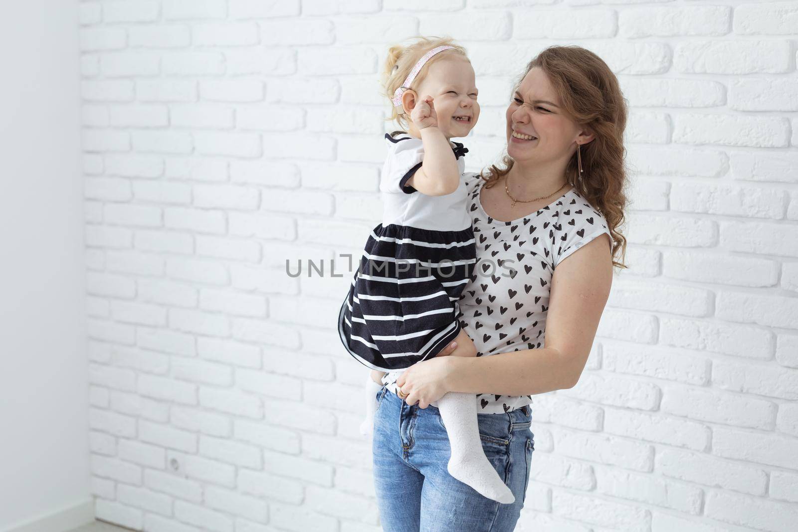Mother holds her child with hearing aids and cochlear implants on white brick wall with copy space and place for advertising . Deaf and health concept by Satura86