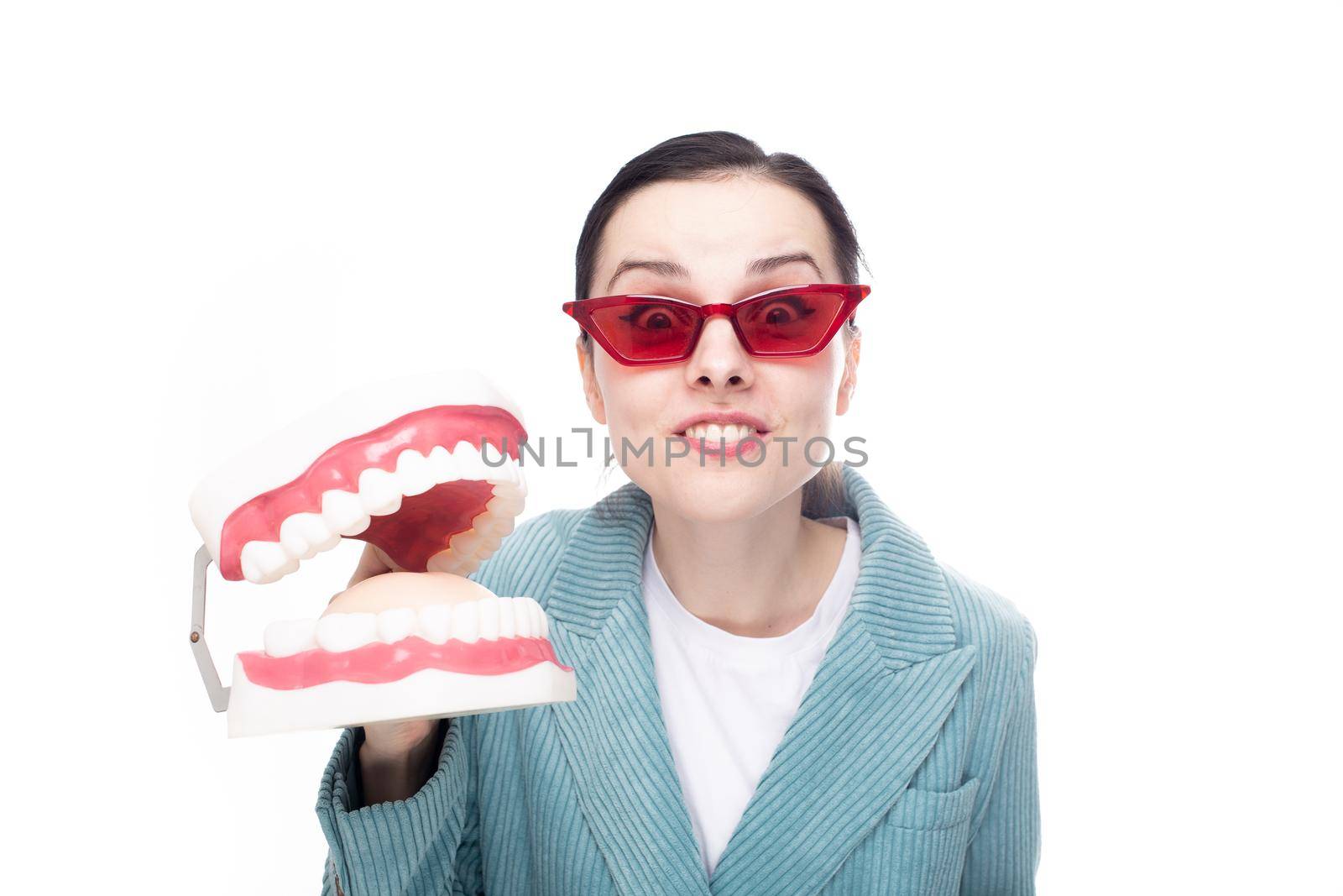 enthusiastic woman in red glasses and corduroy jacket holds a dental jaw in her hand, white background by shilovskaya