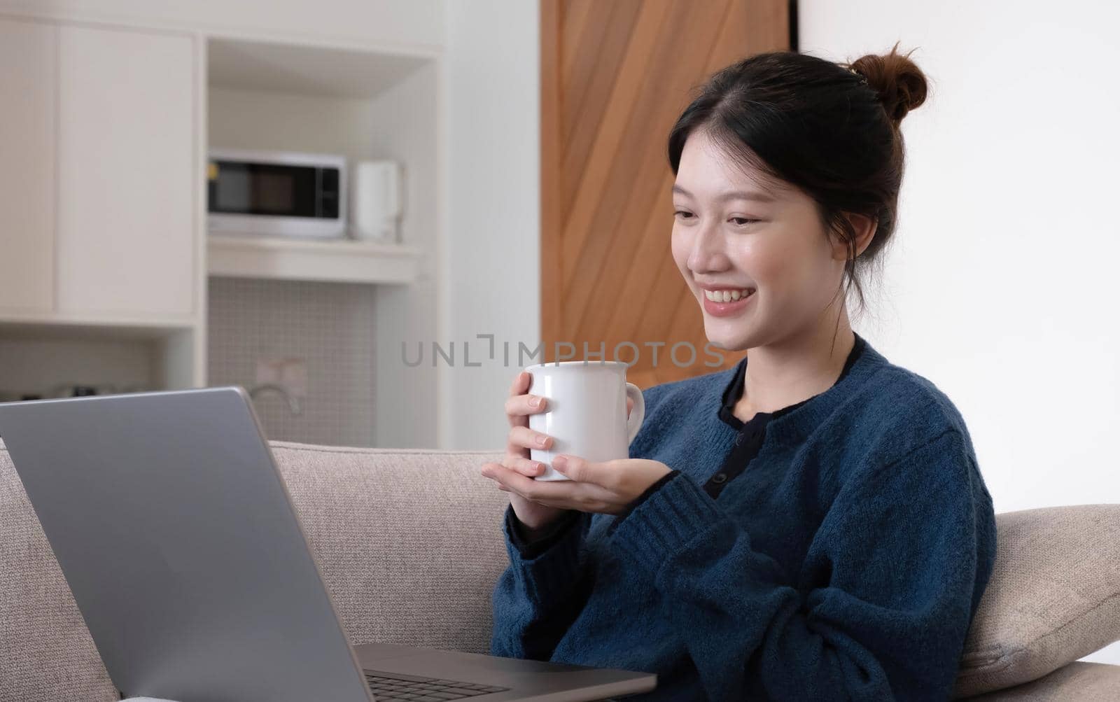 Portrait beautiful young asian woman Working on Laptop Online, Using Internet and hold the cup. Sitting on Sofa at Home, Free Space.