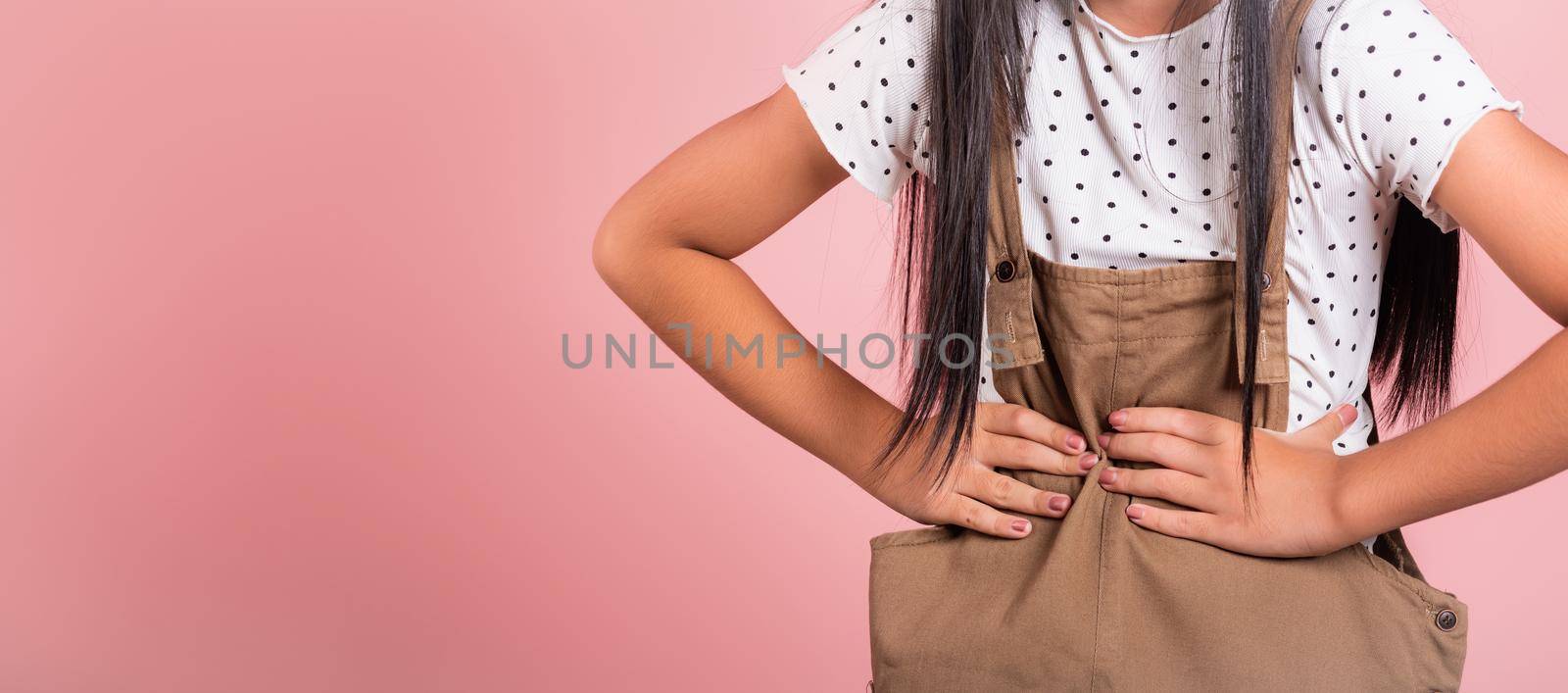 Asian little kid 10 years old suffering from stomach ache at studio shot isolated on pink background, Happy child girl hand hold stomach pain because indigestion, painful illness feeling unwell