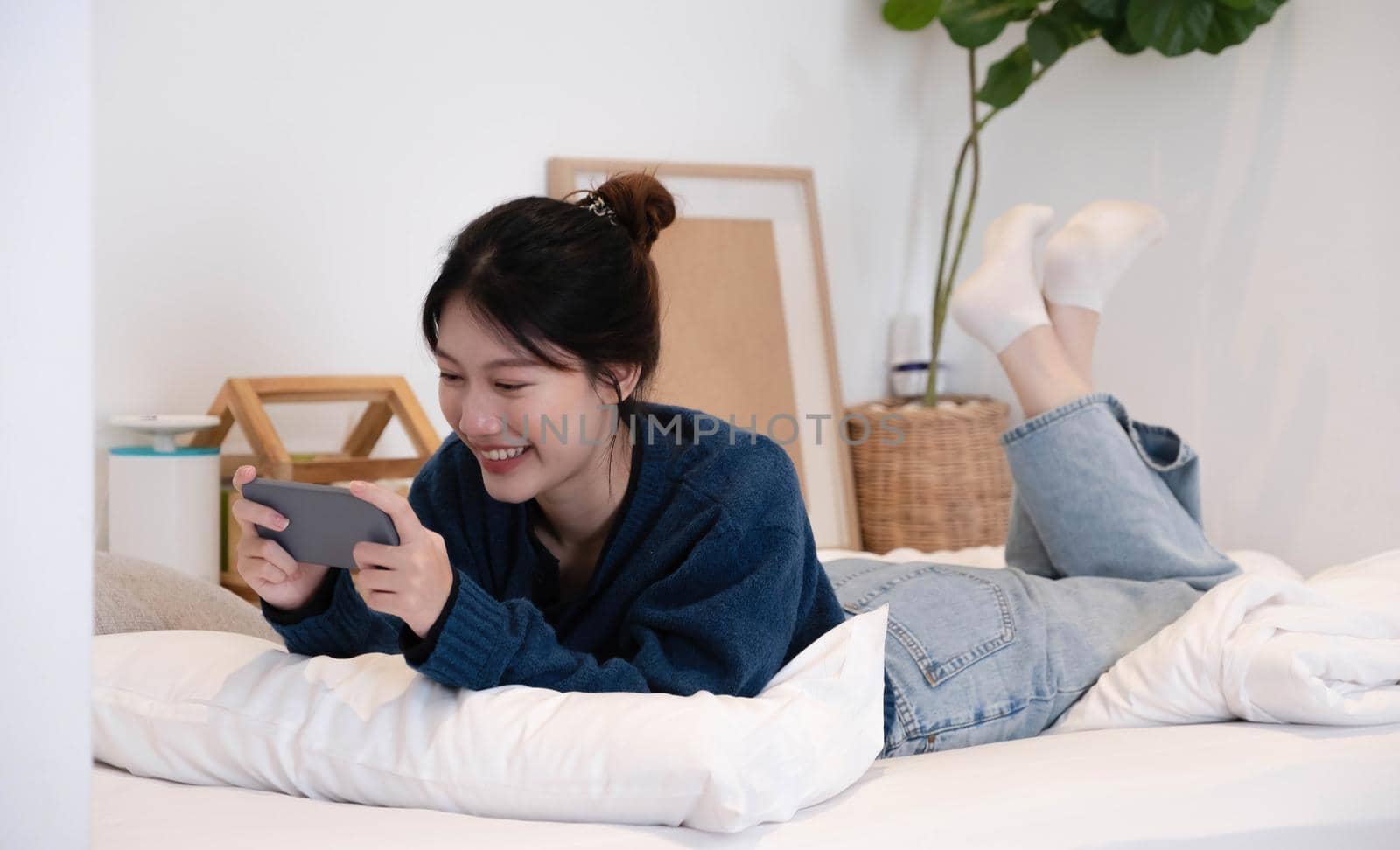 Portrait beautiful young asian woman on a white mattress in the bedroom in the morning.The smartphone is in the hands of women. Lady holding phone. by wichayada