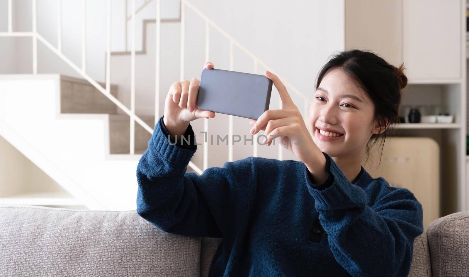Shot of a happy young Asia woman taking selfie with her cellphone while sitting at living room..