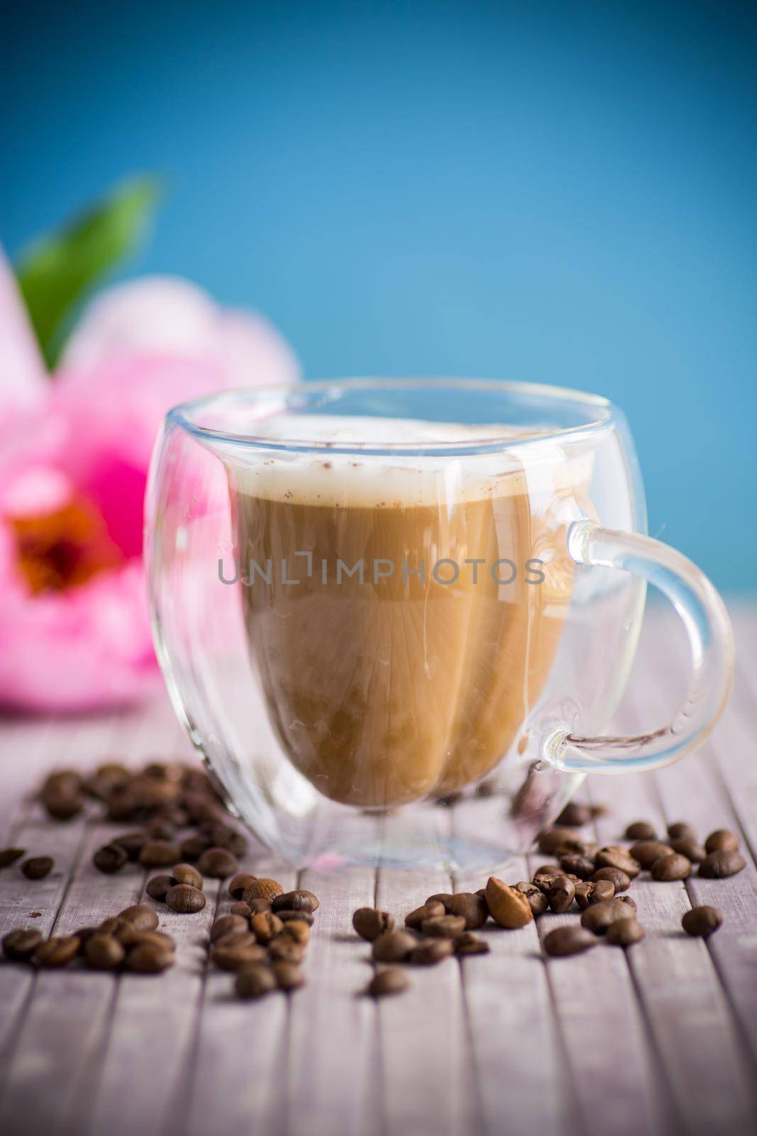 A cup of hot coffee with milk with coffee beans, on a wooden table.