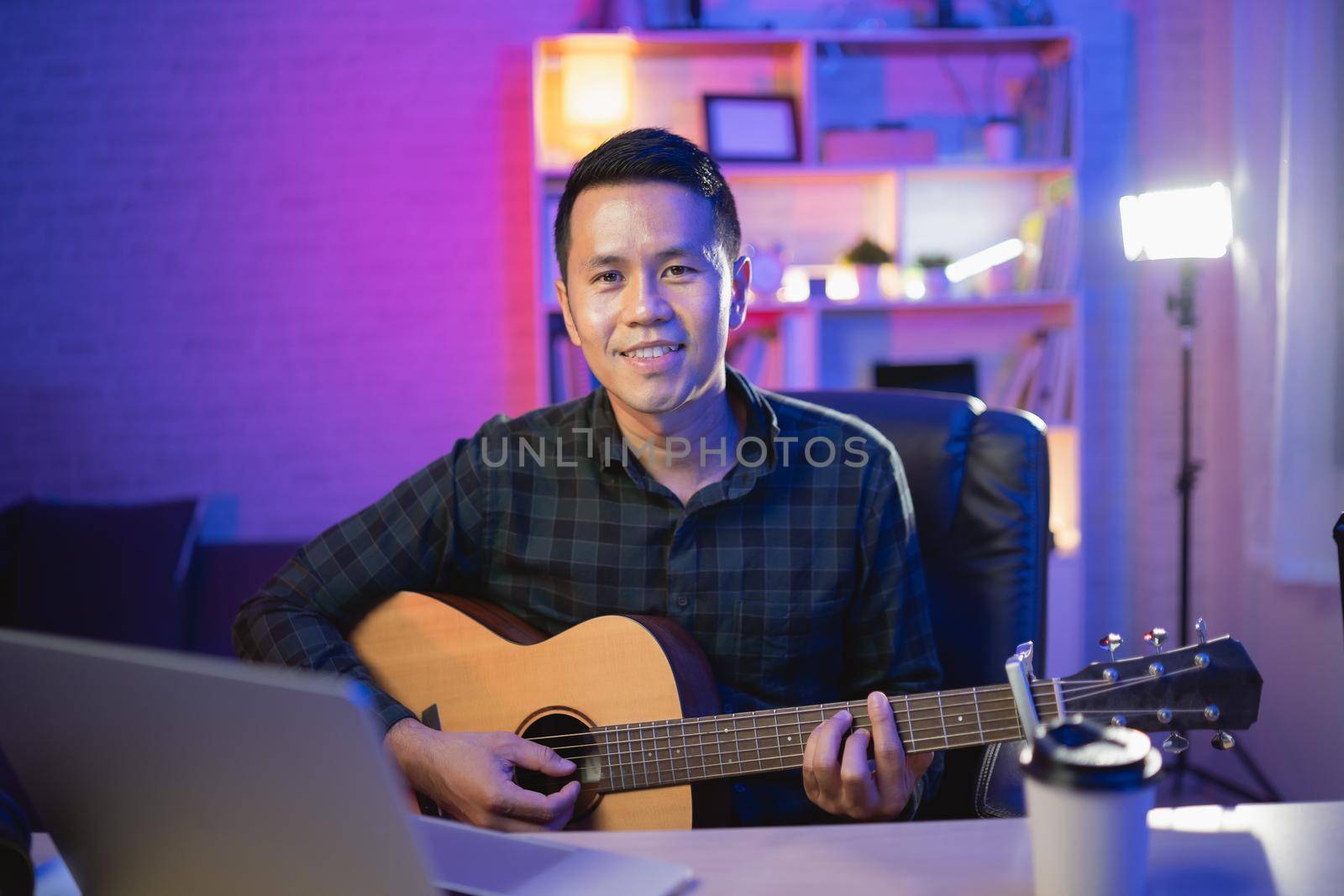 Asian man youtuber live streaming perfomance playing guitar and sing a song. Asian man teaching guitar and singing online. Musician recording music with laptop and playing acoustic guitar. by Wmpix