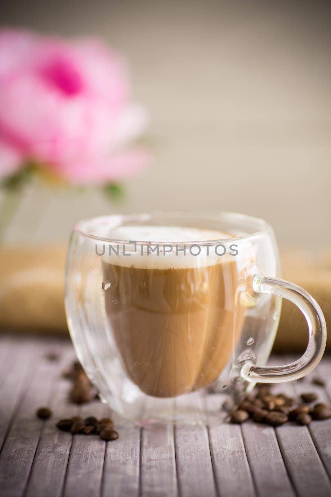 A cup of hot coffee with milk with coffee beans, on a wooden table.