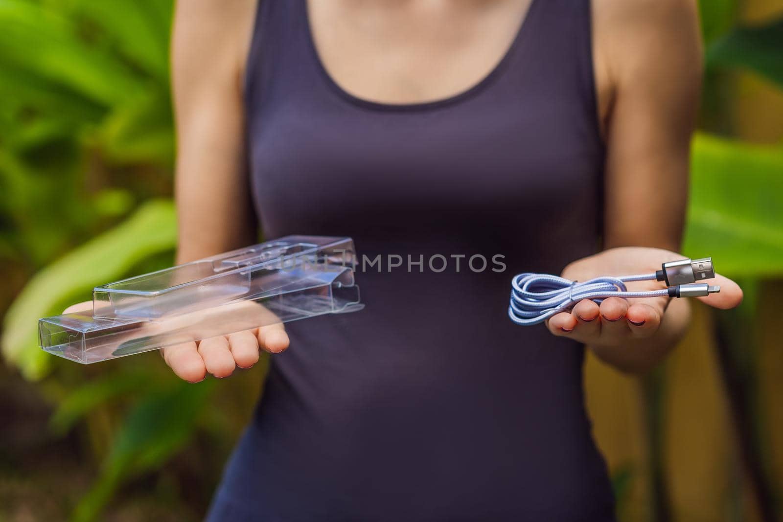Female hands printed a new wire to charge the phone. The wire was packed in a large number of plastic packaging, which will be thrown into the trash. Zero waste concept. Plastic trash concept.