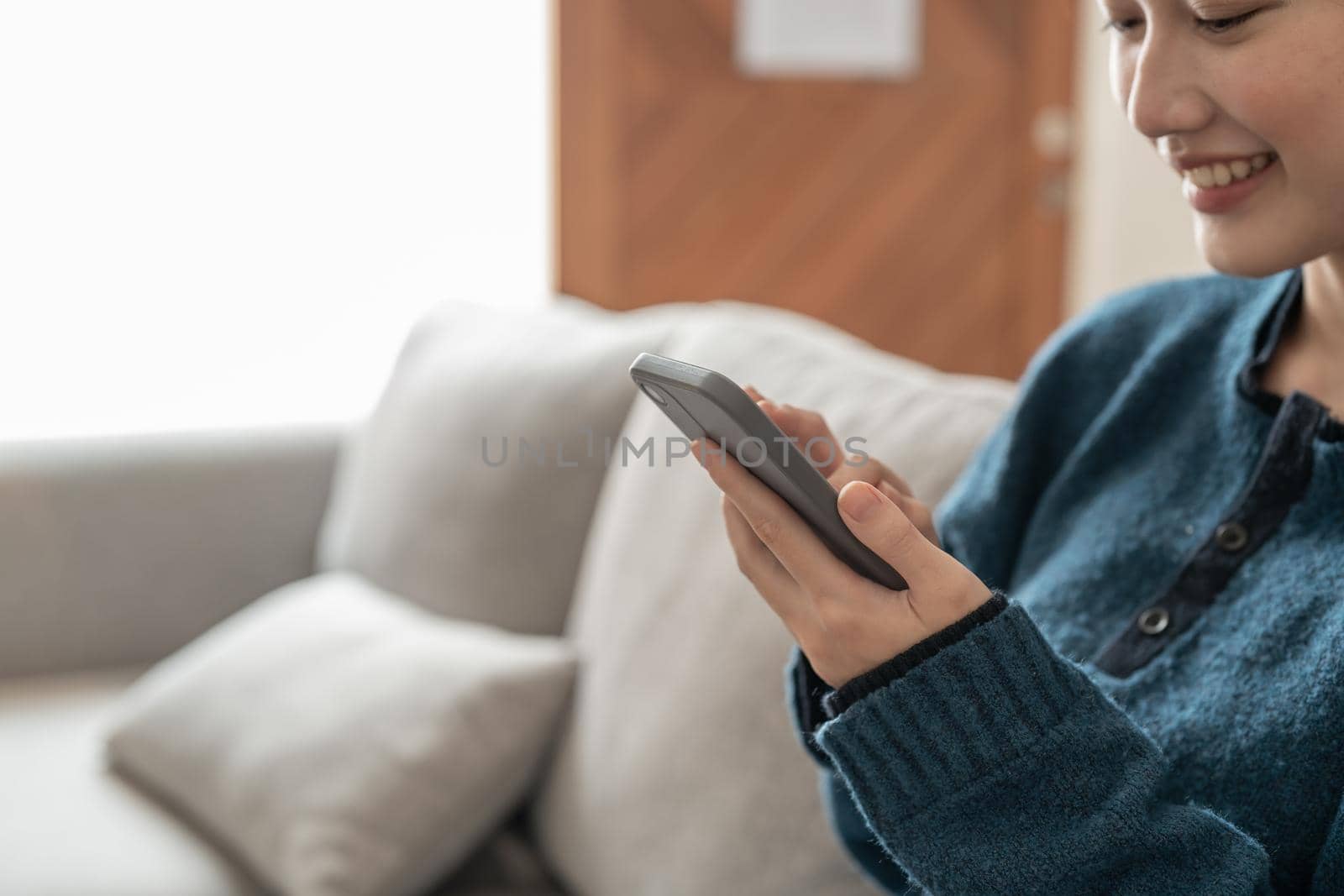Close up cheerful young asian woman using mobile phone while sitting on a couch at home.