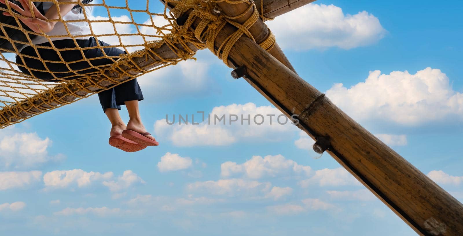 Summer travel at the beach with blue sky and white clouds. Summer vibes. Summer vacations. Relax on vacations. Woman with pink flipflop sit on net rope with enjoy and relax mood on holiday at resort.