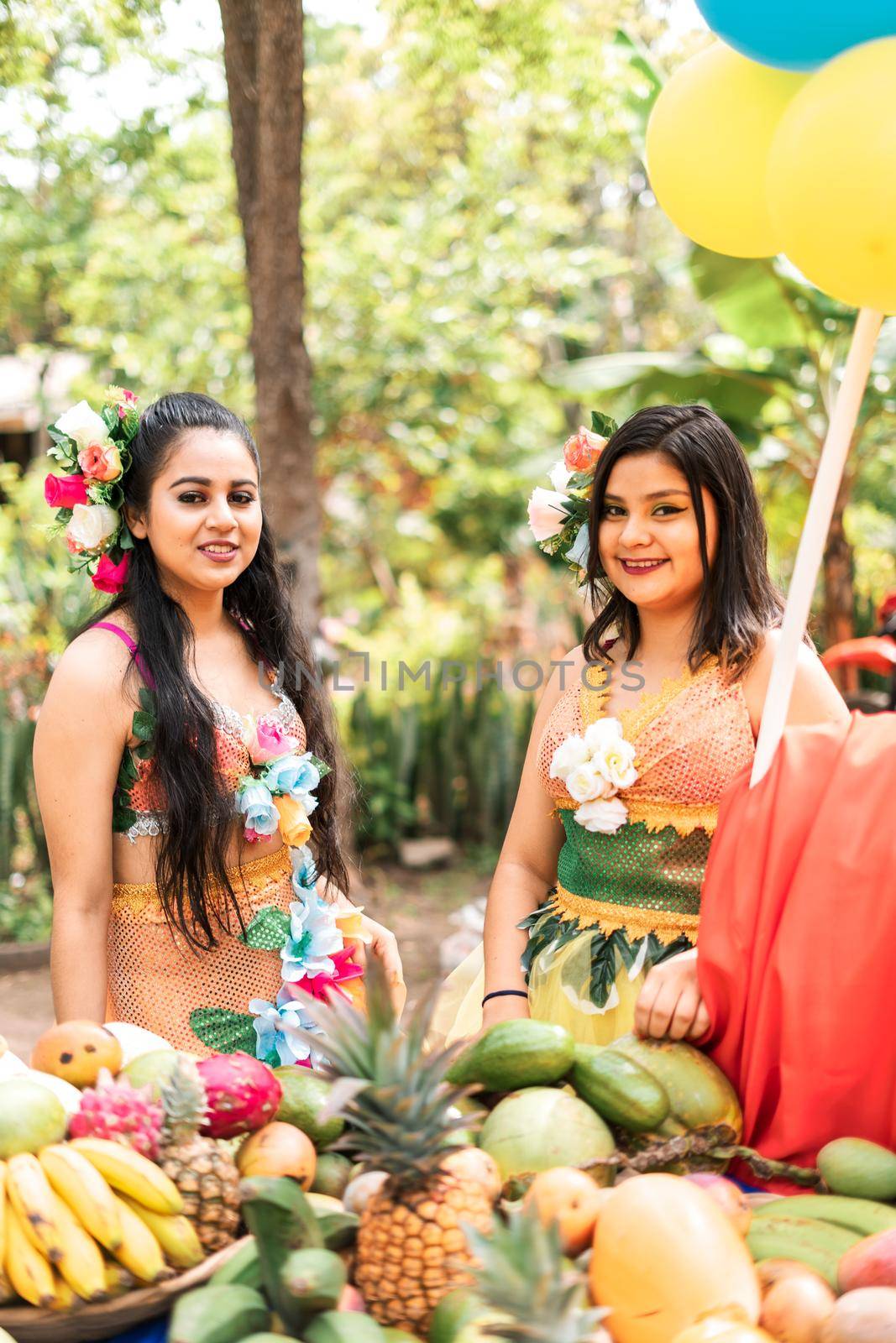Vertical photo of two pretty Latin women in tropical dresses picking fruit during a harvest festival in Masaya by cfalvarez