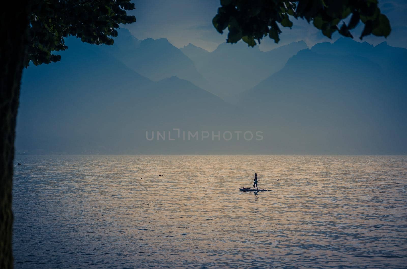 View of mountains Alps, figure silhouette of a man on a surfboard with paddle on the Lake Leman Lake Geneva in Montreux, Swiss Riviera, Vaud canton, Switzerland