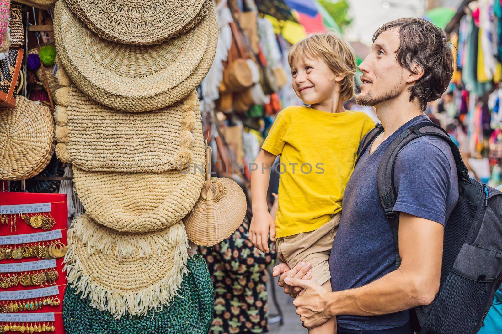 Dad and son at a market in Ubud, Bali. Typical souvenir shop selling souvenirs and handicrafts of Bali at the famous Ubud Market, Indonesia. Balinese market. Souvenirs of wood and crafts of local residents. Traveling with children concept. Kids friendly place.