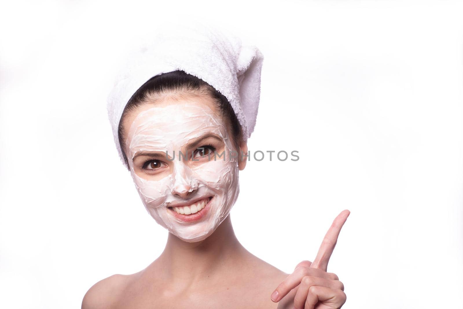 woman in a white towel on her head with a white cosmetic mask on her face, white background, close-up portrait. High quality photo