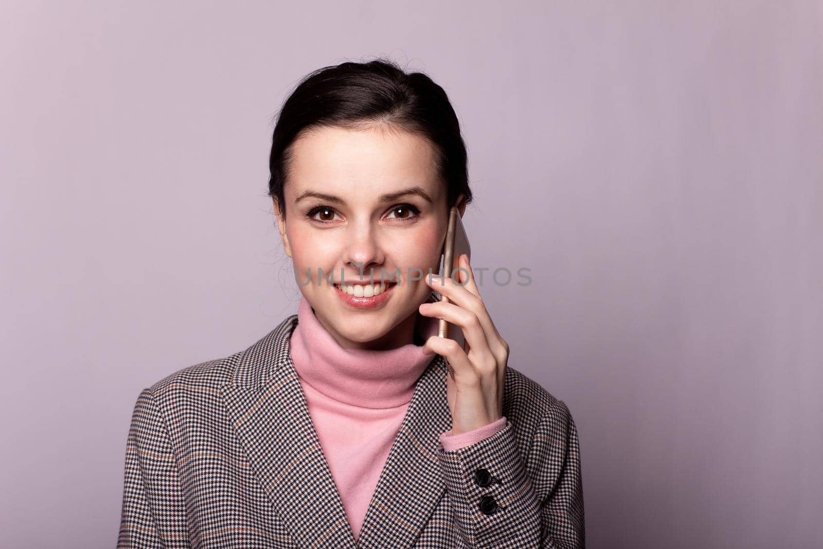 woman in a pink turtleneck, gray jacket, for sight communicates on the phone on a gray background by shilovskaya