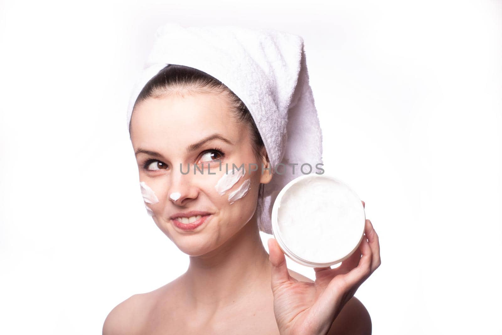a woman with a white towel on her head and a cream on her face holds a package of cream in her hands. High quality photo