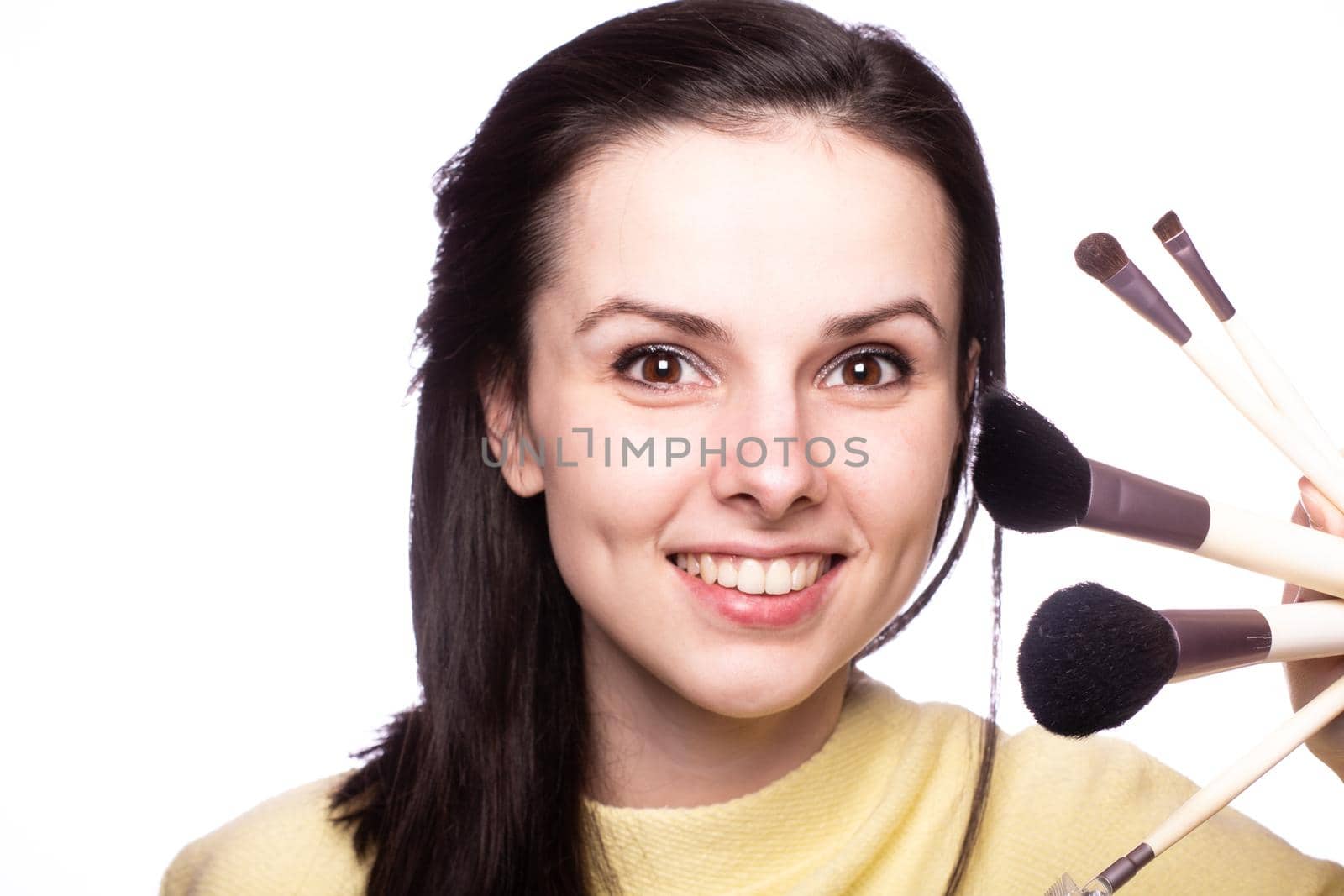 brunette woman in yellow sweater holding makeup brushes by shilovskaya