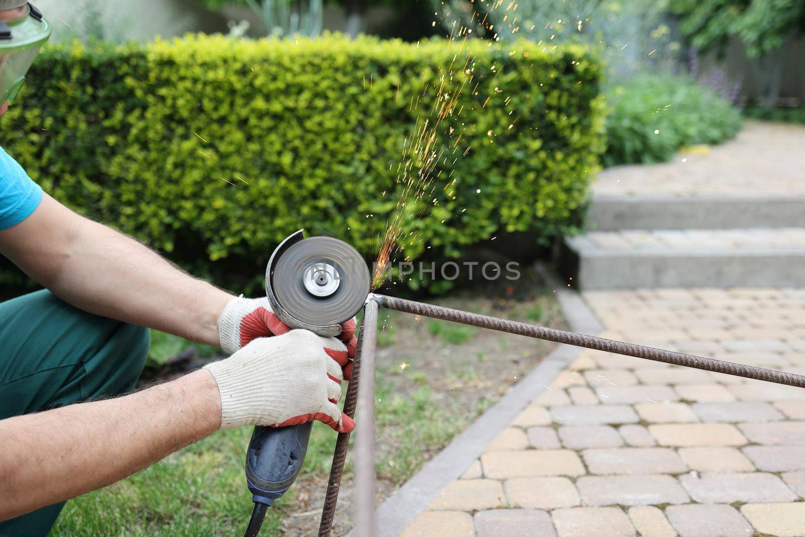 male hands in thick protective gloves cut an iron rod, sparks fly close-up. Cutting a metal rod with a burst of sparks. male repair work with electric tool in the garden.
