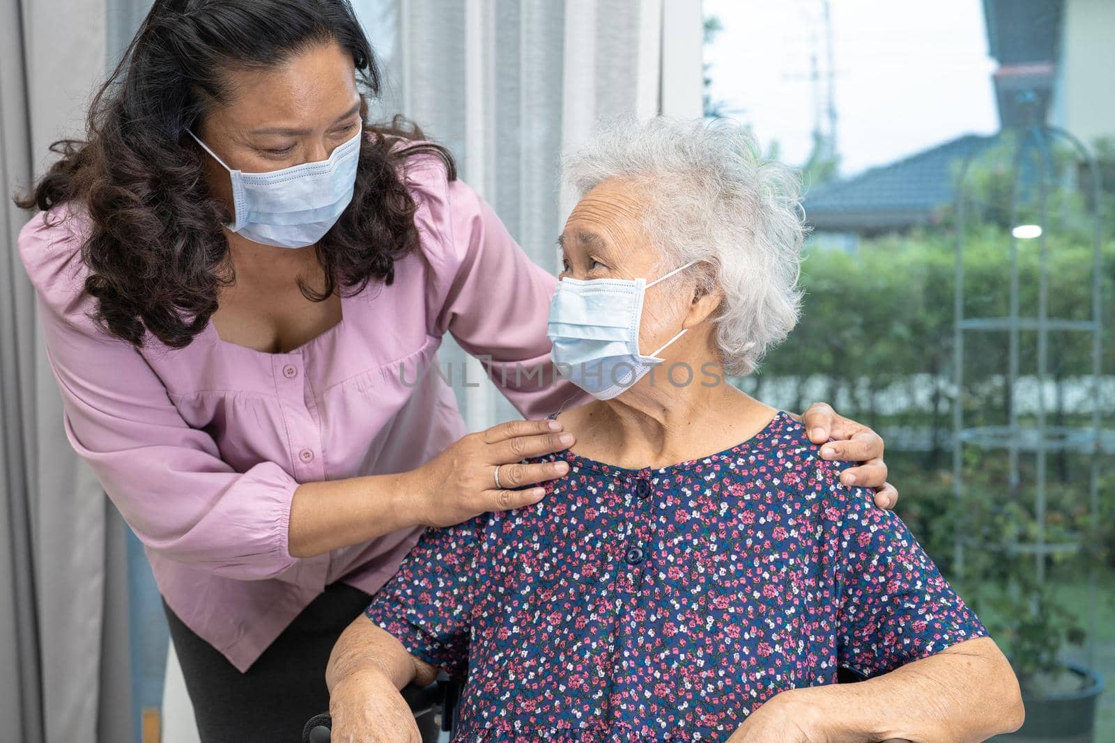 Caregiver help Asian senior or elderly old lady woman sitting on wheelchair and wearing a face mask for protect safety infection Covid19 Coronavirus. by pamai