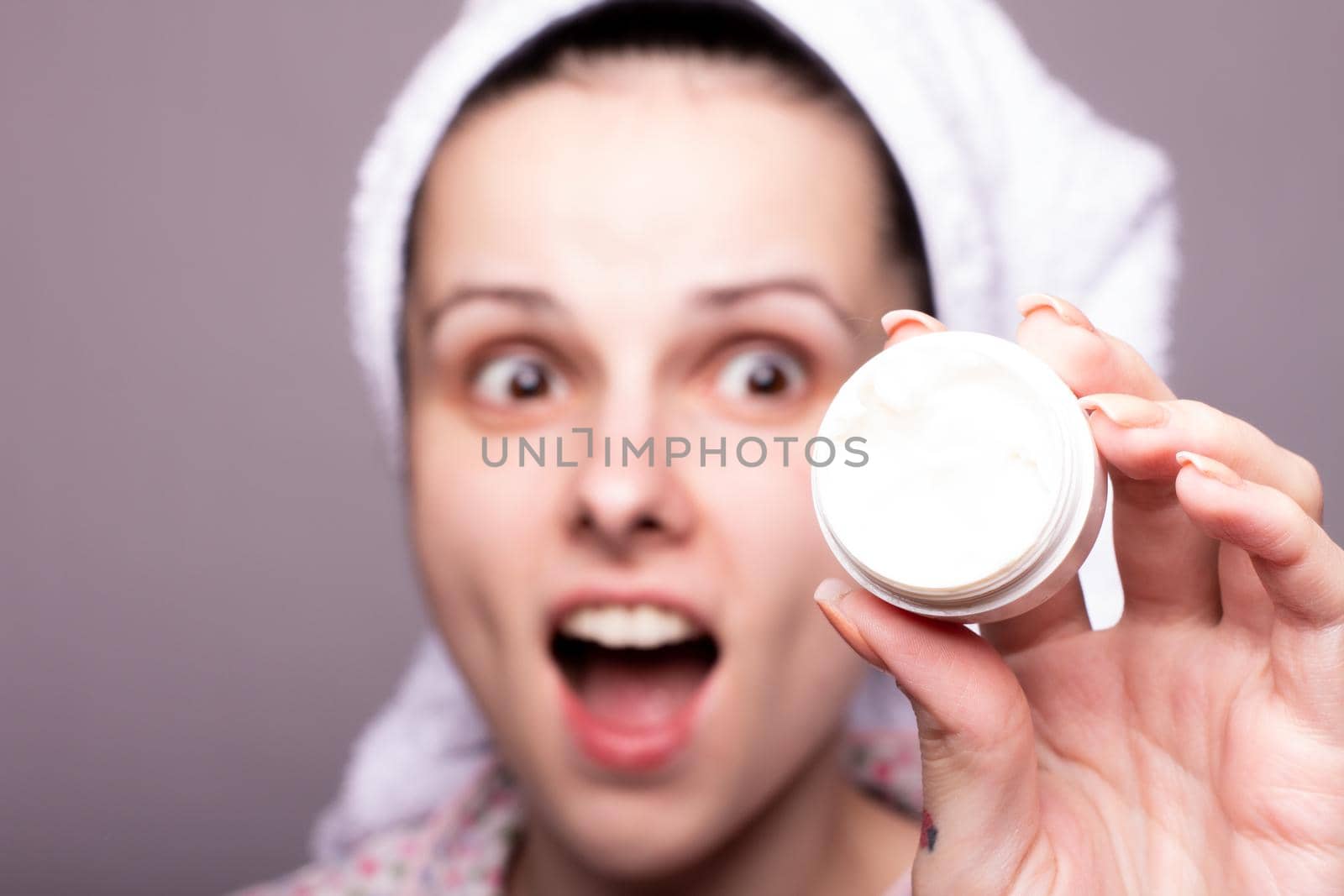 a brunette woman in a towel on her head holds a package of cosmetic cream in front of her by shilovskaya