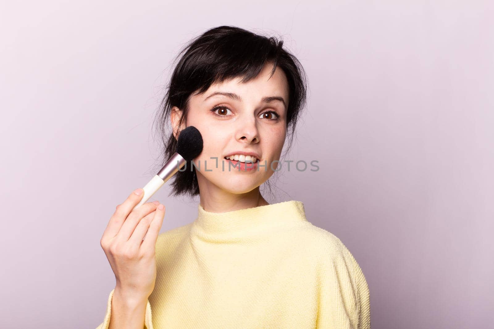 attractive woman in a yellow sweater does makeup with a brush by shilovskaya