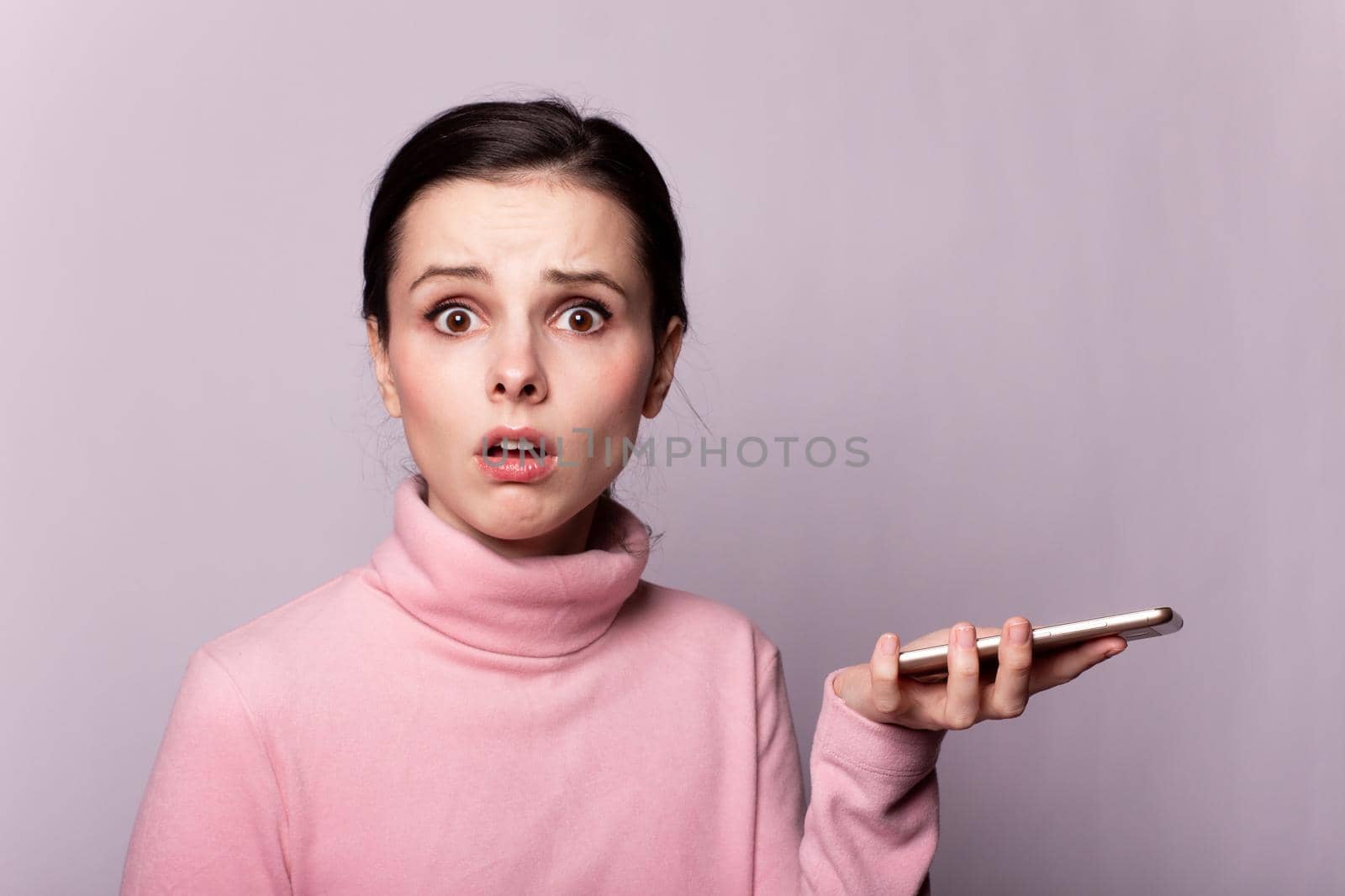 beautiful girl in a pink turtleneck talking on the phone on a gray background by shilovskaya