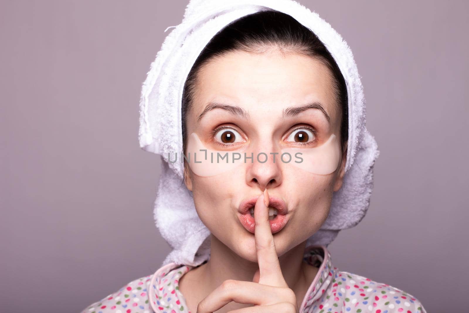 woman with cosmetic patches under her eyes, white towel on her head, gray background close-up. High quality photo