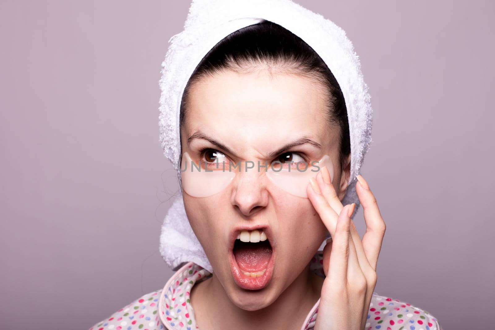 woman with cosmetic patches under her eyes, white towel on her head, gray background close-up by shilovskaya