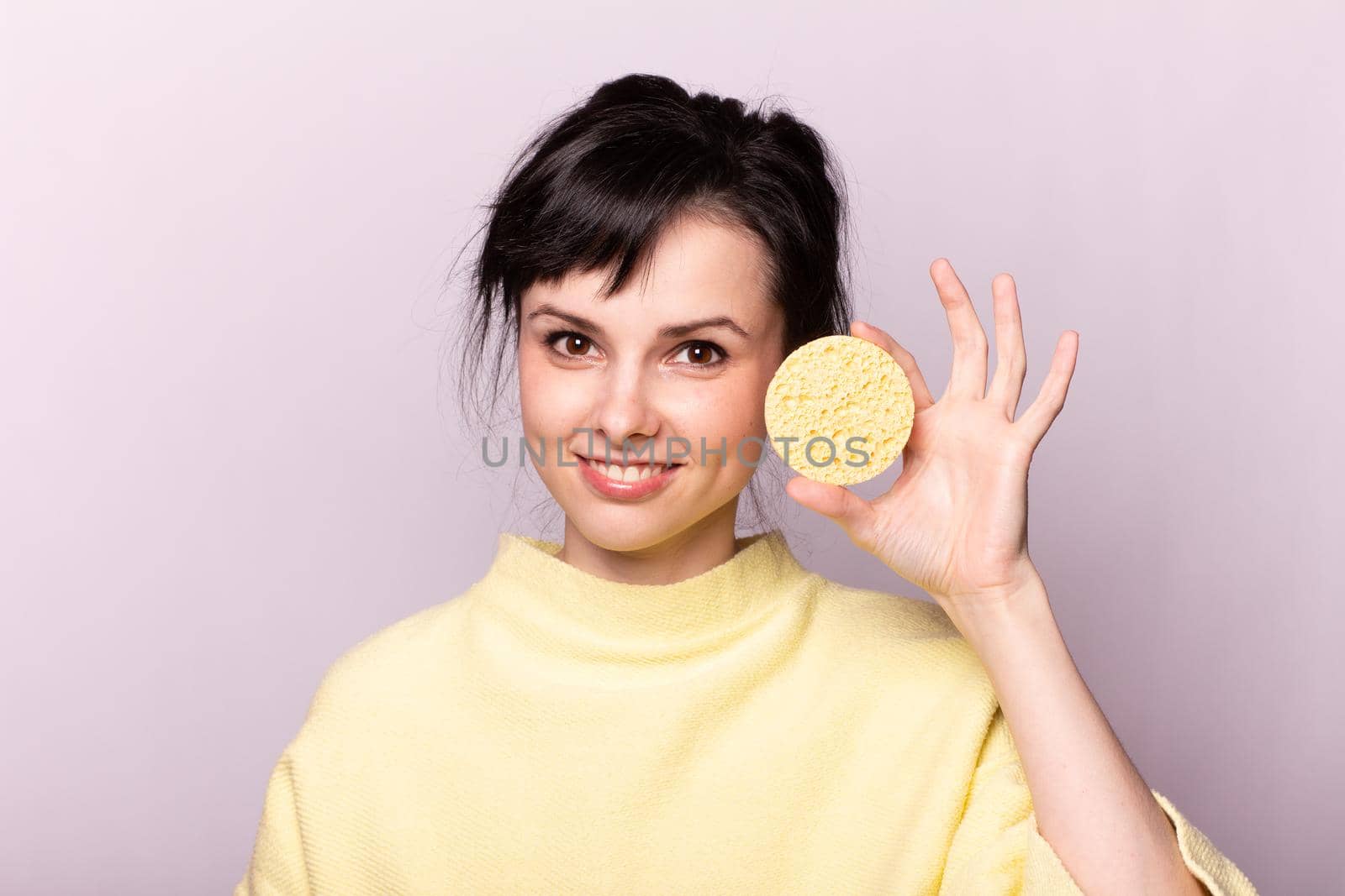 cute brunette woman in a yellow sweater holds a cosmetic sponge in her hands. High quality photo