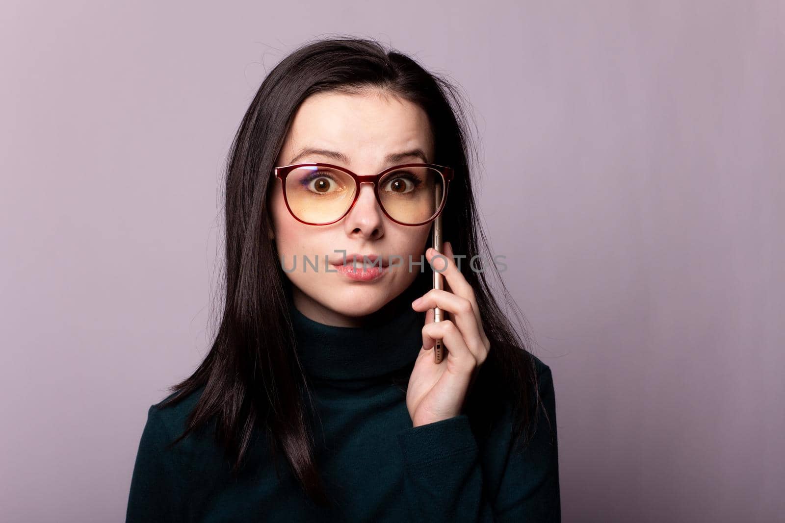 woman in a green turtleneck and glasses for sight communicates on the phone, portrait on a gray background by shilovskaya