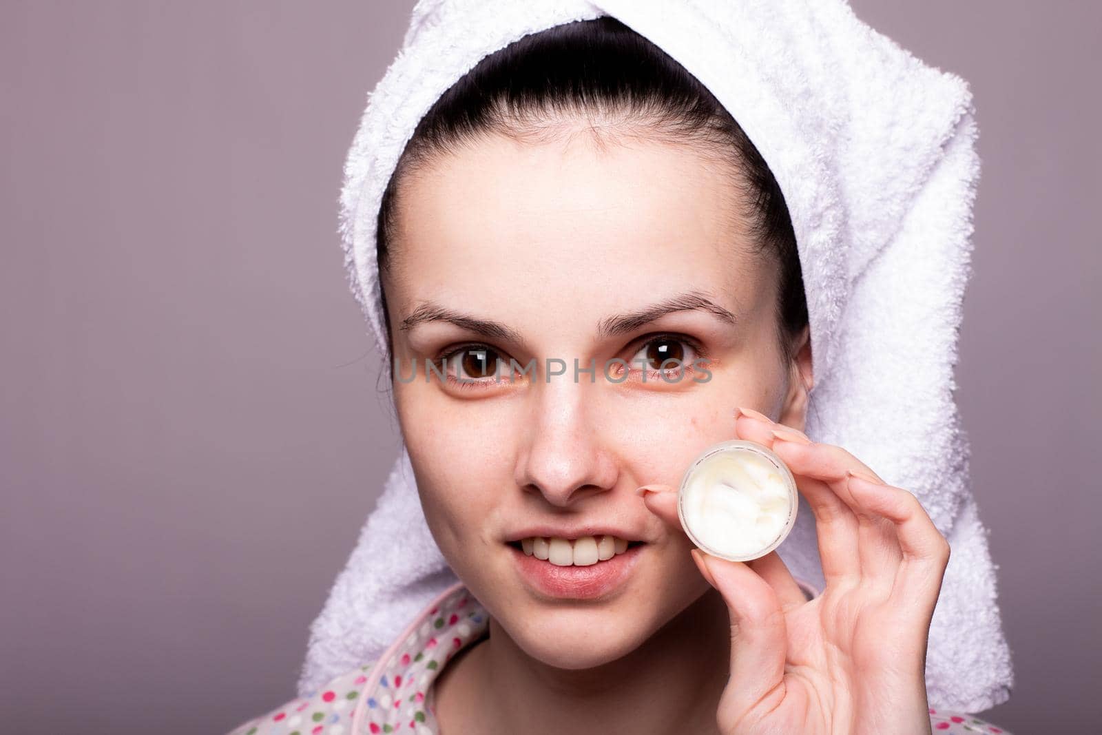a brunette woman in a towel on her head holds a package of cosmetic cream in front of her. High quality photo