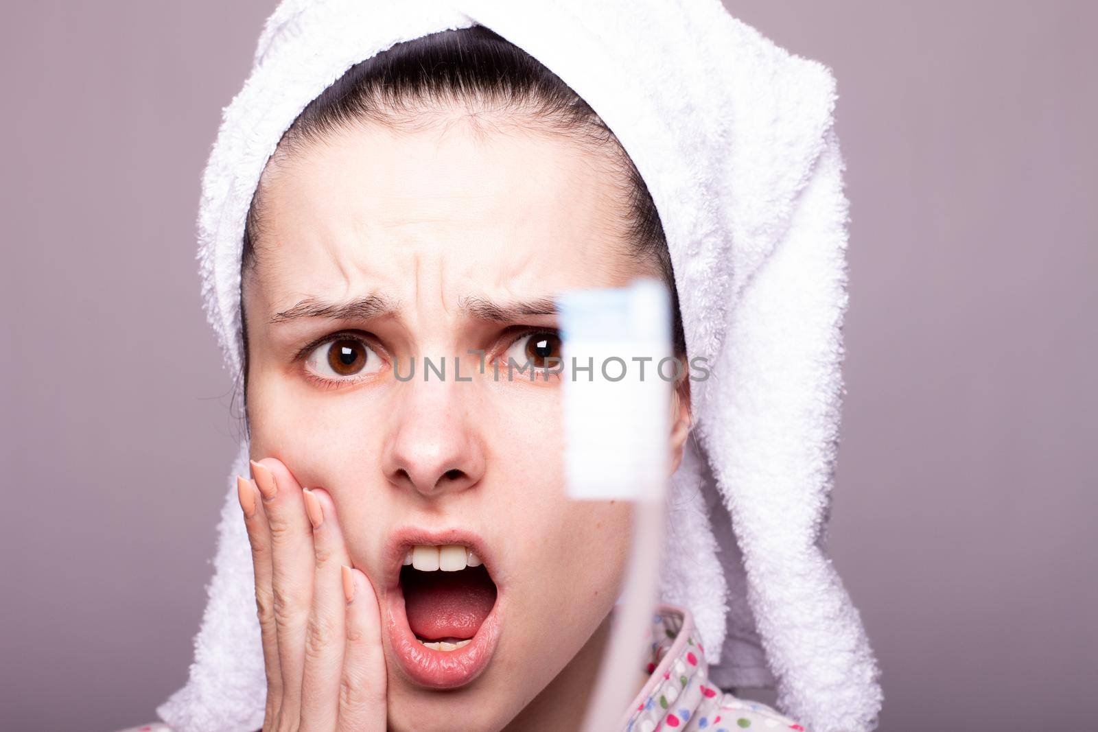 a woman in a towel on her head holds a toothbrush in front of her, gray background, close-up. High quality photo
