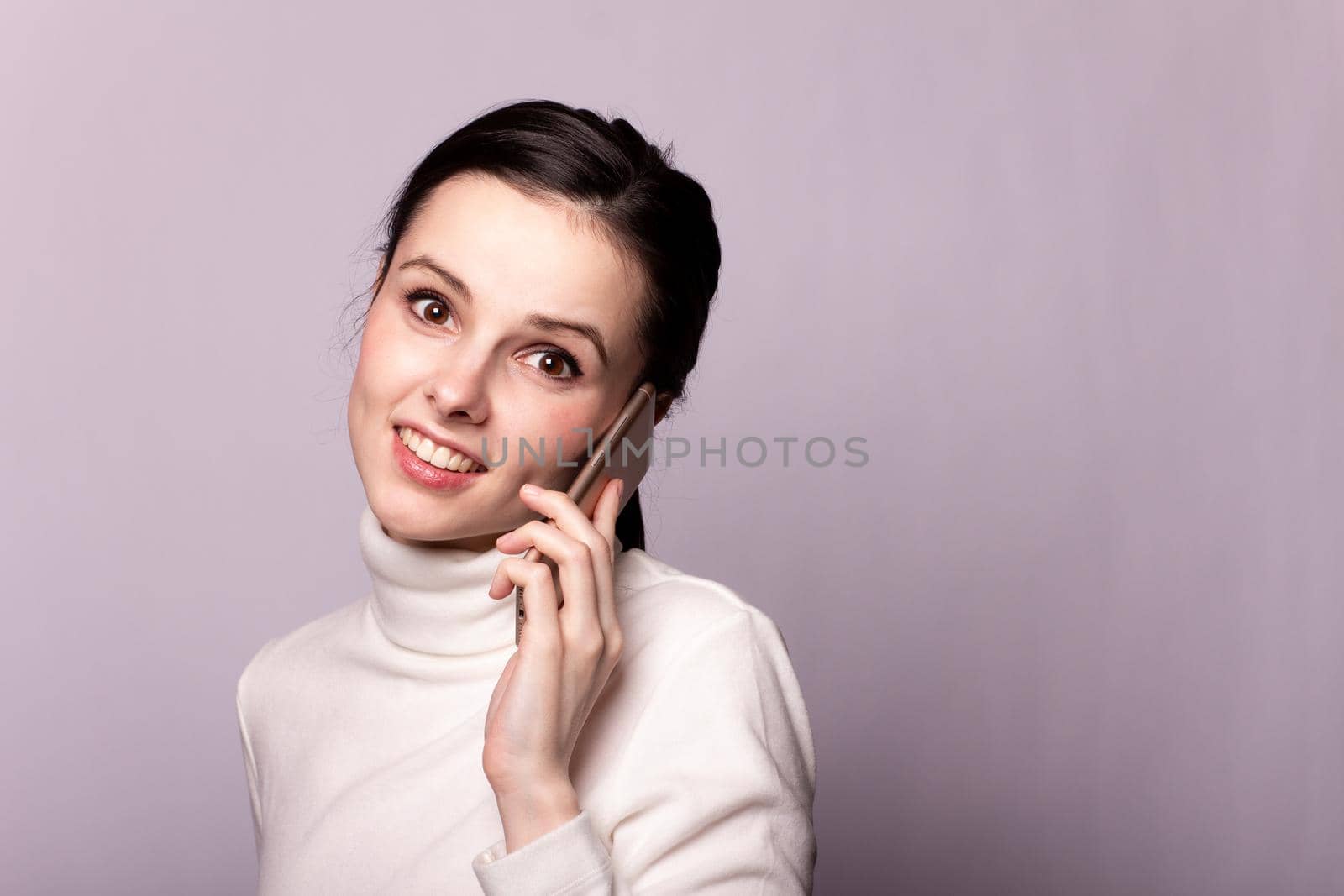 woman in a white turtleneck talking on the phone, portrait on a gray background by shilovskaya