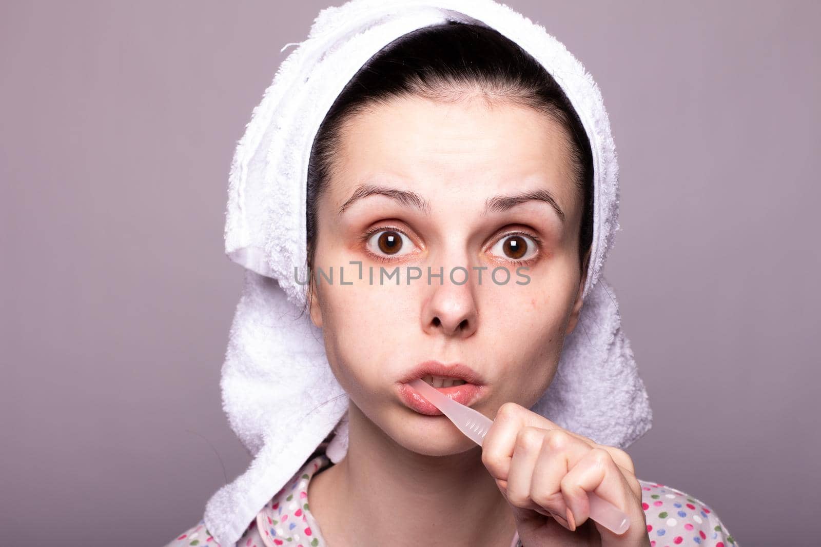 a woman in a towel on her head brushes her teeth, gray background, close-up. High quality photo