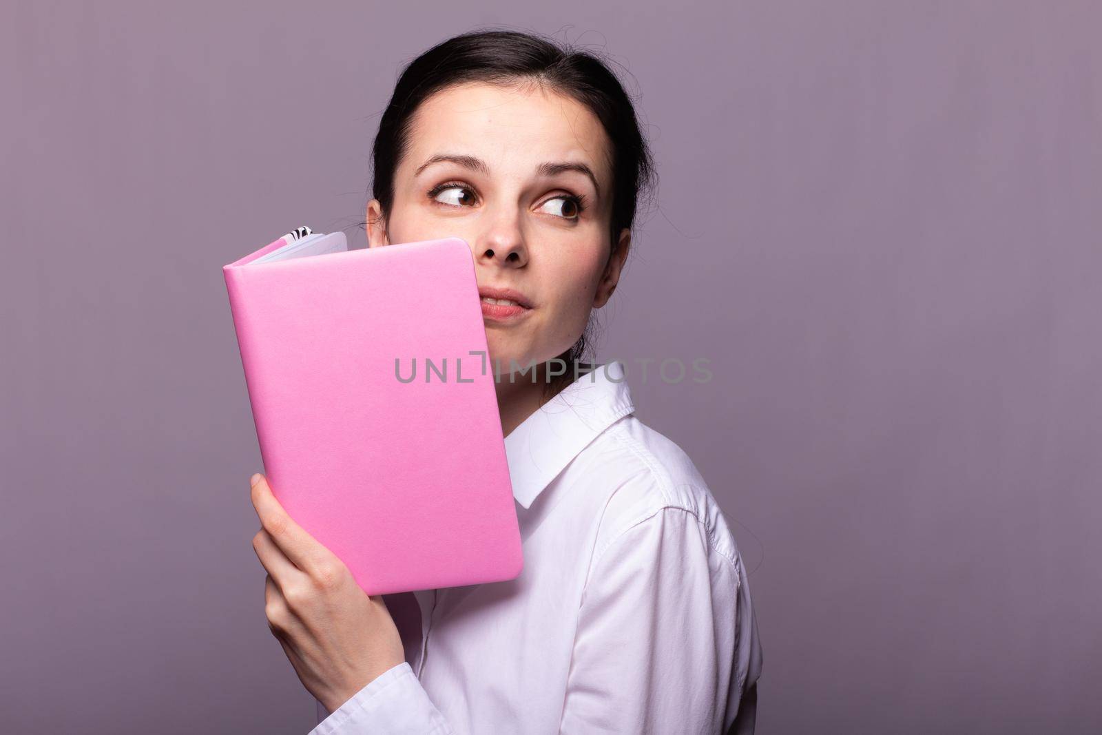 woman in a white shirt holds a pink notebook in her hands. High quality photo