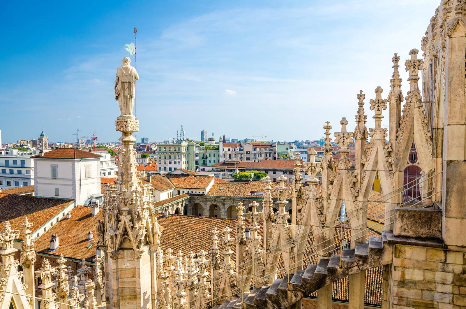 White marble statues on roof of famous Duomo di Milano Cathedral and top aerial view of Milan city with blue sky, Lombardy, Italy