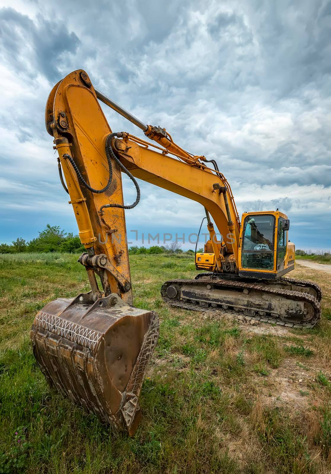 A parked yellow excavator on a meadow at sunset