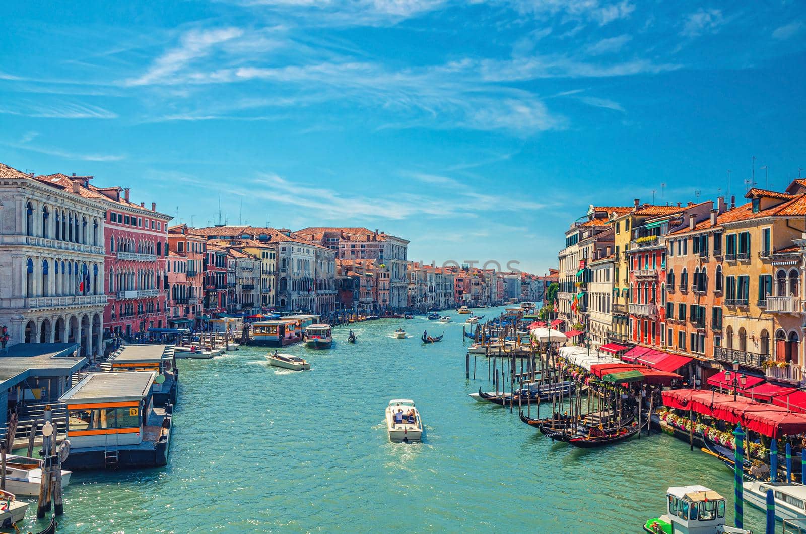 Venice cityscape with Grand Canal waterway. View from Rialto Bridge. Gondolas, boats, vaporettos docked and sailing Canal Grande. Venetian architecture colorful buildings. Veneto Region, Italy.