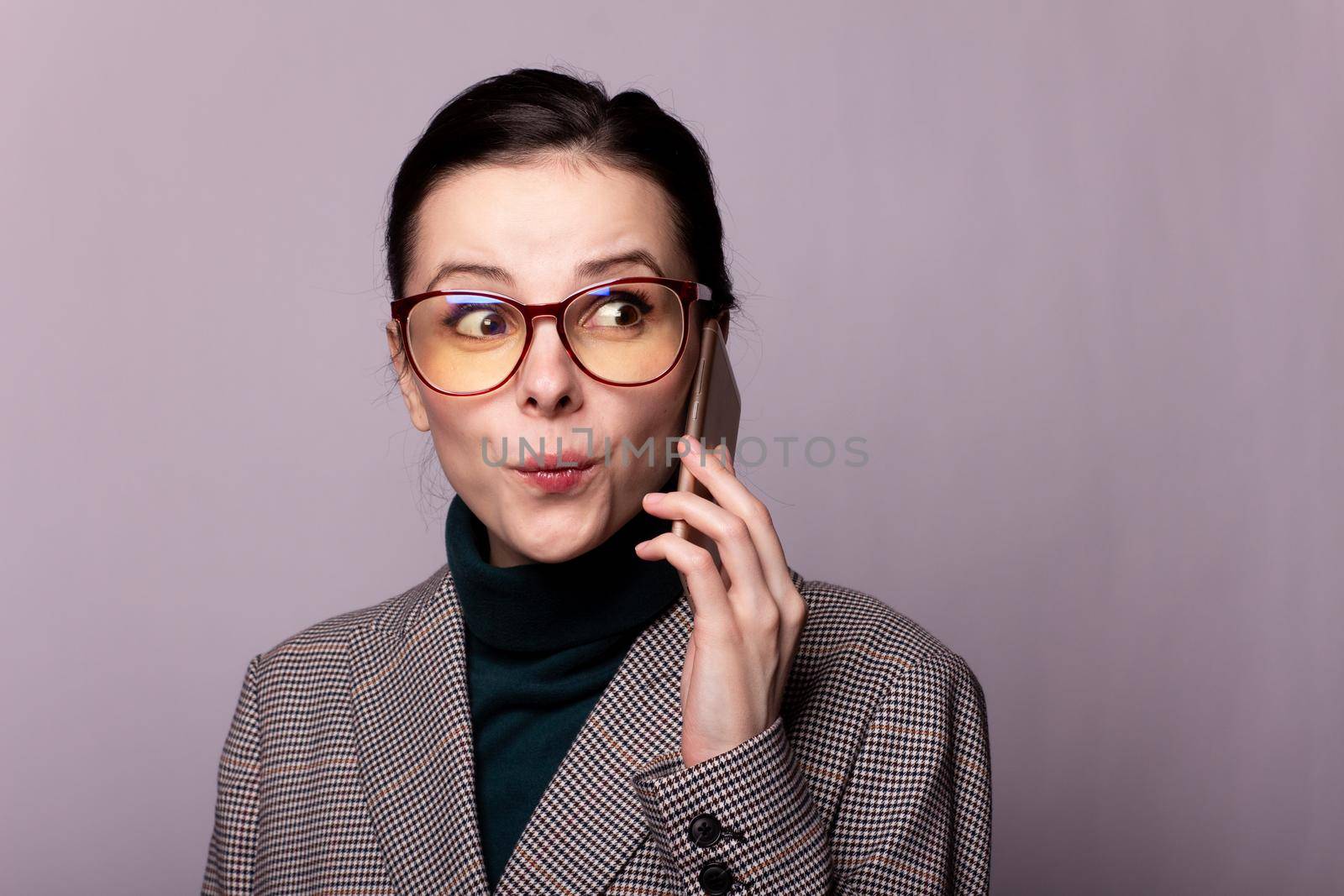 woman in a green turtleneck, jacket, glasses talking on the phone portrait on a gray background. High quality photo