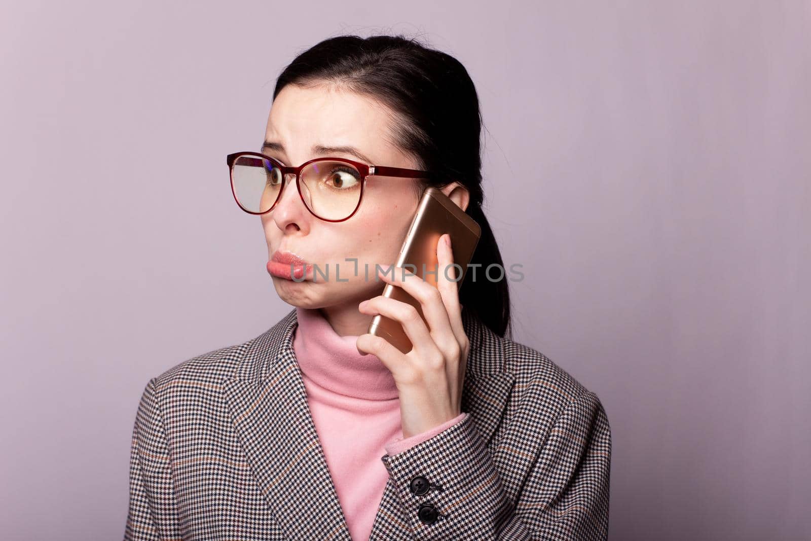 woman in a pink turtleneck, gray jacket, glasses for sight communicates on the phone on a gray background. High quality photo