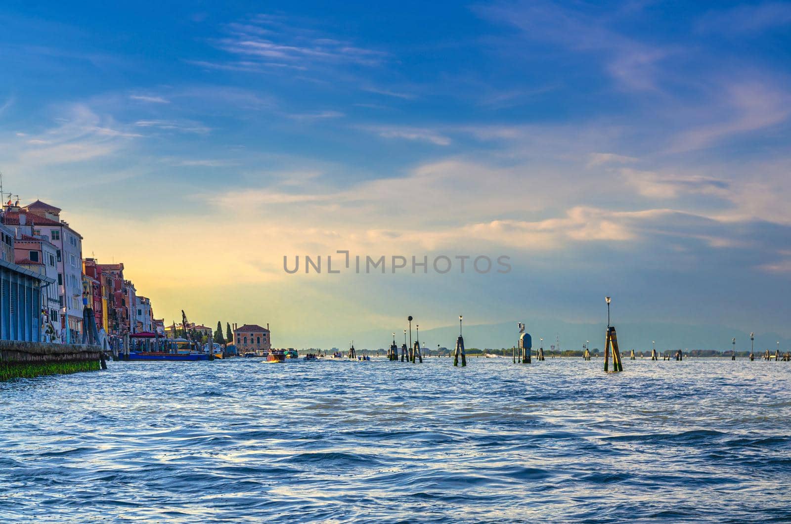 Yacht boats racing sailing on water of Venetian lagoon between wooden poles near Venice city coastline, island at horizon, Veneto region, Northern Italy