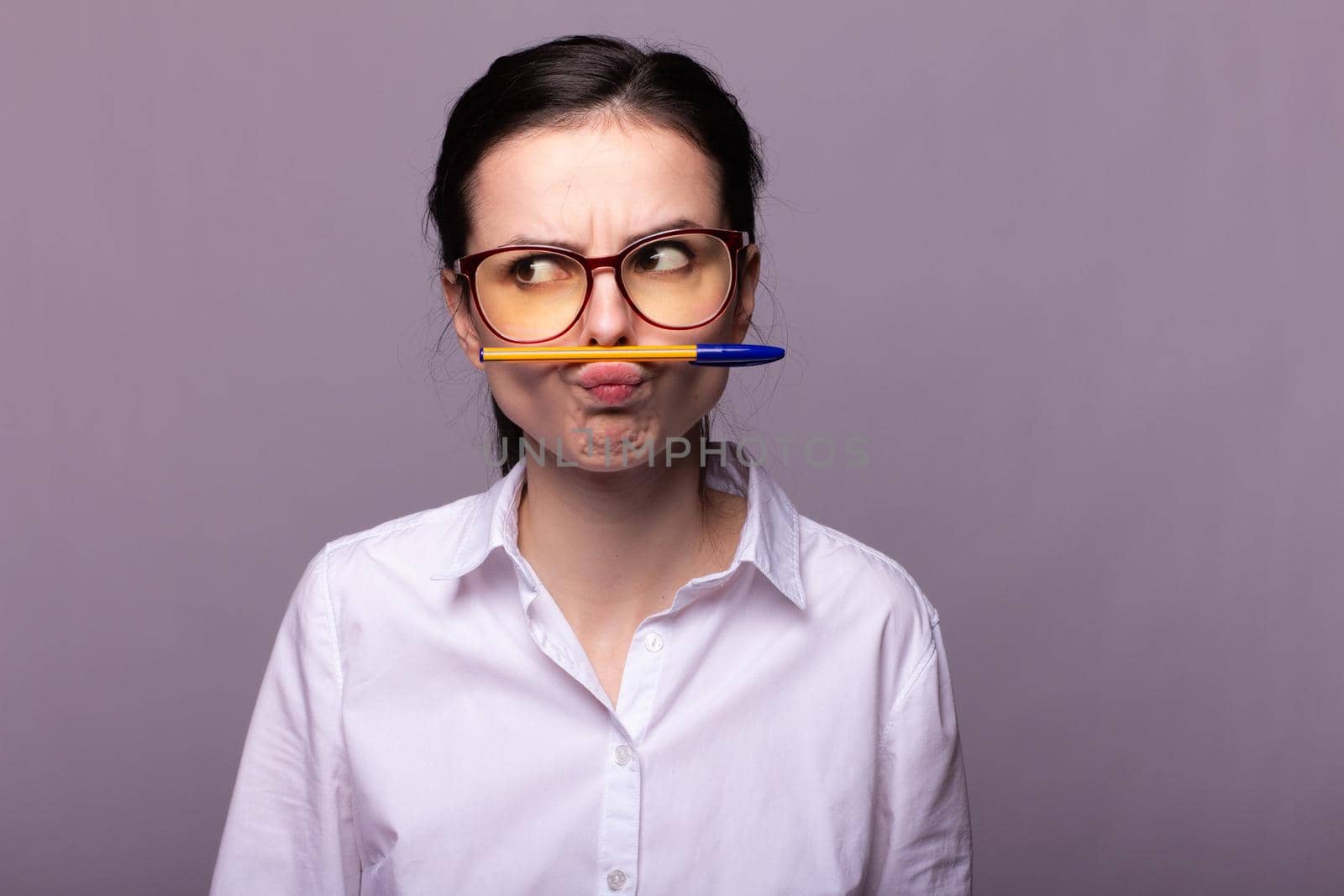 woman in a white shirt and glasses holds a pen with her mouth. High quality photo