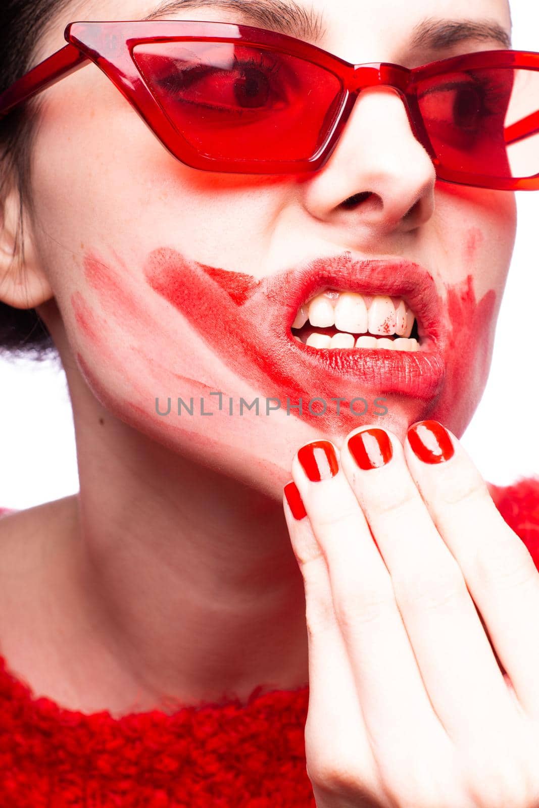brunette woman in red glasses smears red lipstick on her face, red nails, white background by shilovskaya